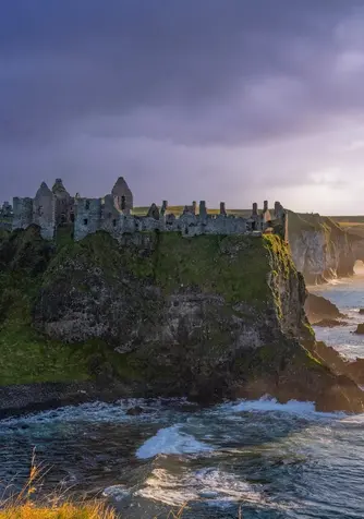 Dunluce Castle ruins perched on dramatic cliffs along the Causeway Coast at sunset.