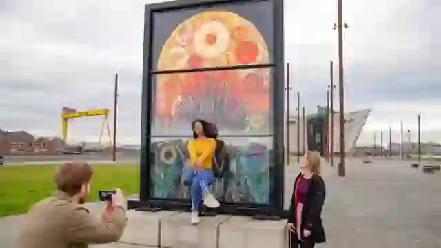 Menschen fotografieren die „Glass of Thrones”-Buntglasfenster in der Nähe des Titanic Belfast.