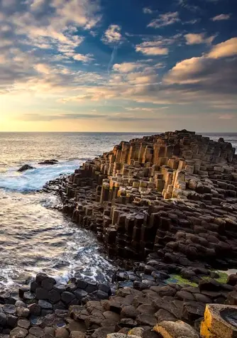 Sunset over the Giant’s Causeway with hexagonal basalt columns and waves along the rugged Antrim coast.