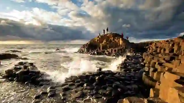 Visitors exploring the Giant's Causeway's basalt columns as Atlantic waves crash beneath dramatic skies.