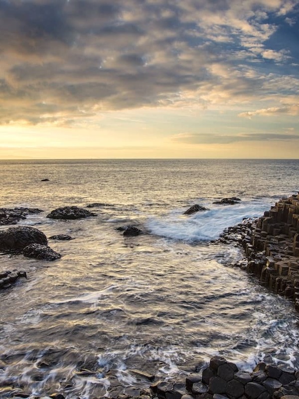 Sunset over the Giant’s Causeway with hexagonal basalt columns and waves along the rugged Antrim coast.