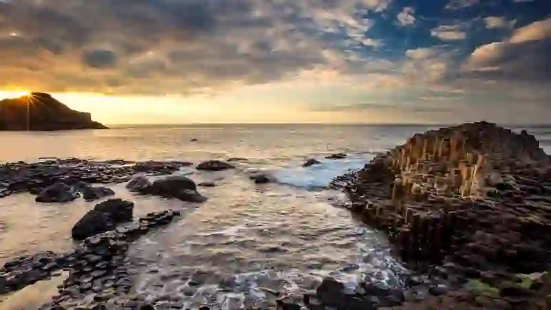 Sunset over the Giant’s Causeway with hexagonal basalt columns and waves along the rugged Antrim coast.