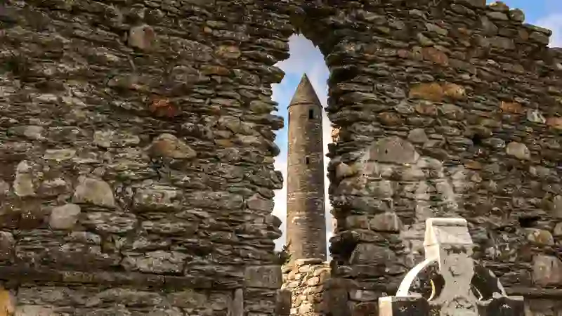 Glendalough round tower framed by the stone arch of a ruined monastic building.