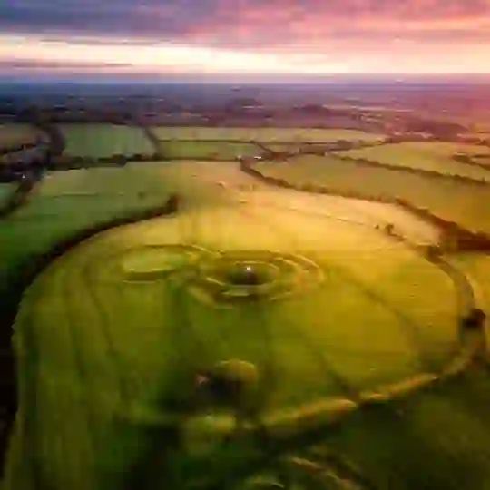 Aussicht über die Erdwerke des Hill of Tara in der Grafschaft Meath bei Sonnenuntergang, umgeben von grünem Ackerland.