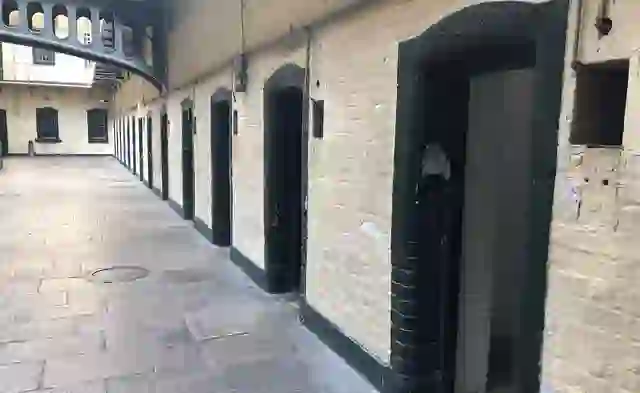 Ground-level row of prison cells inside Kilmainham Gaol with heavy doors and iron walkways above.
