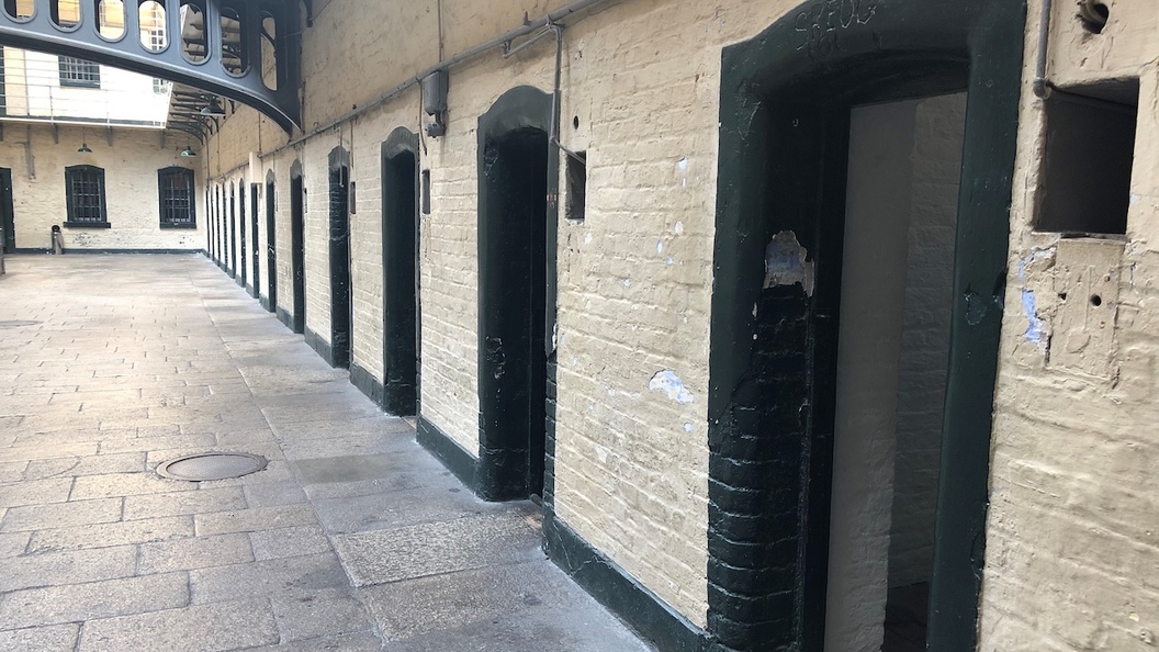 Ground-level row of prison cells inside Kilmainham Gaol with heavy doors and iron walkways above.