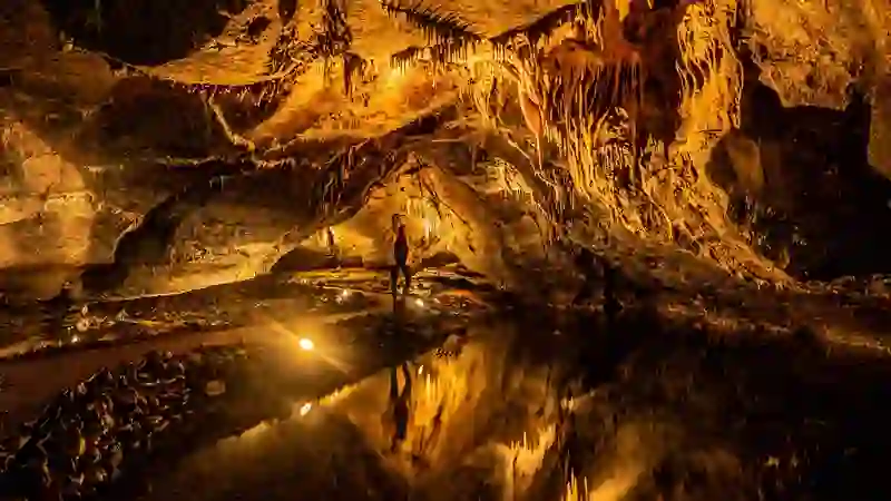 Mitten in den Marble Arch Caves steht ein Besucher, umgeben von beleuchteten Stalaktiten und glitzernden unterirdischen Wasserbecken in der Grafschaft Fermanagh.