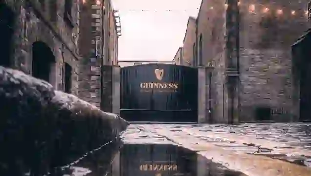 Guinness brewery gate at St James’s Gate in Dublin, reflected in wet cobblestones between historic stone buildings.