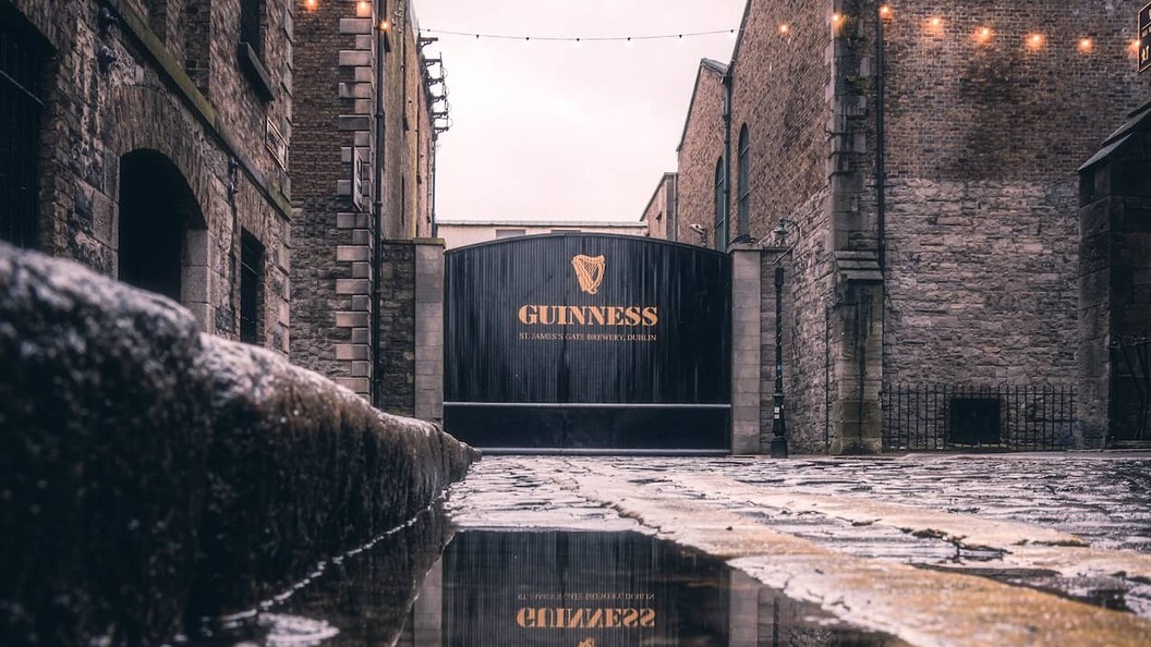 Guinness brewery gate at St James’s Gate in Dublin, reflected in wet cobblestones between historic stone buildings.