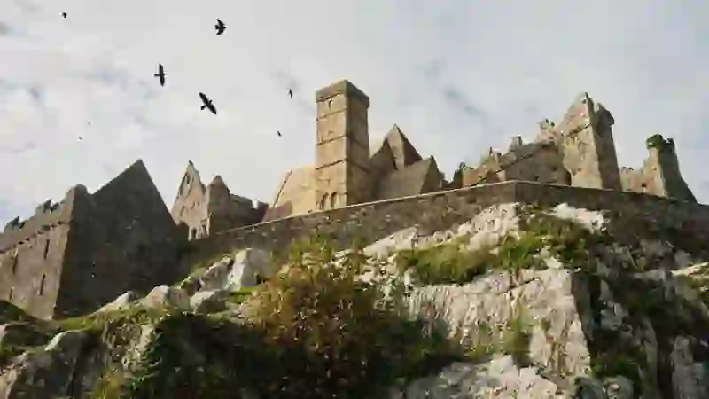 La Roca de Cashel, en el condado de Tipperary, encaramada en unos acantilados de piedra caliza bajo un cielo nublado y con pájaros sobrevolándola