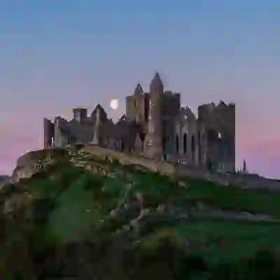 The Rock of Cashel at dusk, with a full moon rising behind the medieval ruins on a green hill in County Tipperary.