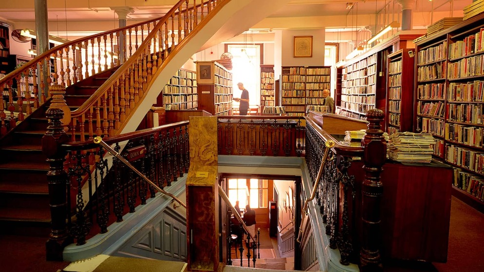 Eine reich verzierte Holztreppe und mit Büchern gesäumte Galerien im Inneren der Linen Hall Library, Belfast.