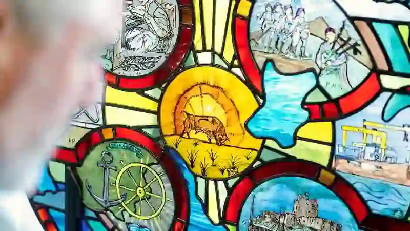 Un visitante contempla una vibrante vidriera que muestra leyendas irlandesas y escenas marítimas y portuarias.