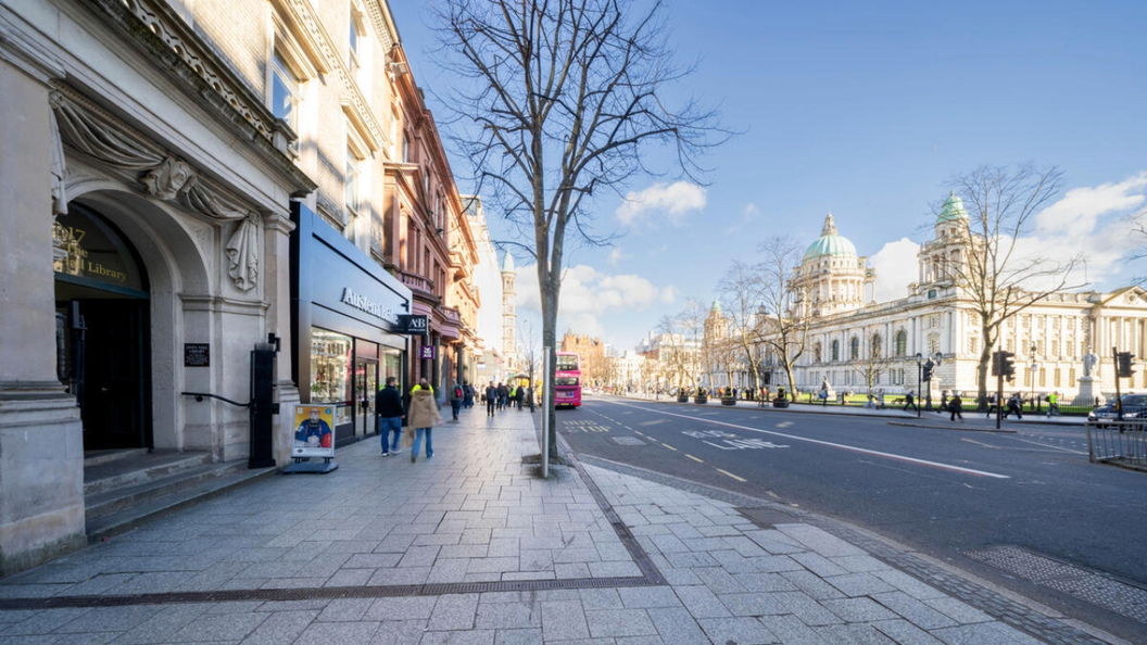 El Ayuntamiento de la Ciudad de Belfast visto desde Donegall Square con peatones caminando por una acera soleada.