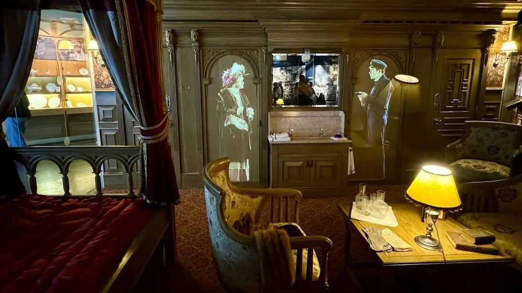Nachbildung einer First-Class-Kabine im Stil der damaligen Zeit im Titanic Belfast mit Vintage-Möbeln und projizierten Figuren.