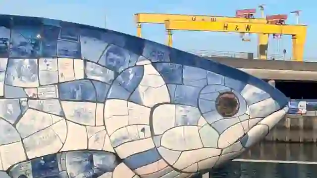 Nahaufnahme der Mosaik-Skulptur Big Fish von Belfast mit den Kränen von Harland & Wolff im Hintergrund.