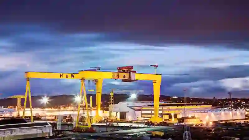 Die legendären gelben Werftkräne von Harland & Wolff, die vor dem tiefblauen Abendhimmel in Belfast erleuchten.