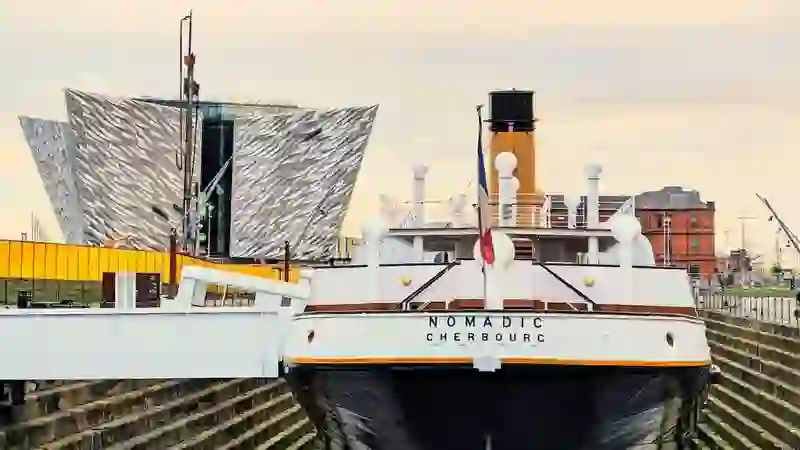 Die SS Nomadic, die im Trockendock vor Anker liegt, dahinter emporragend das moderne Titanic Belfast-Gebäude.