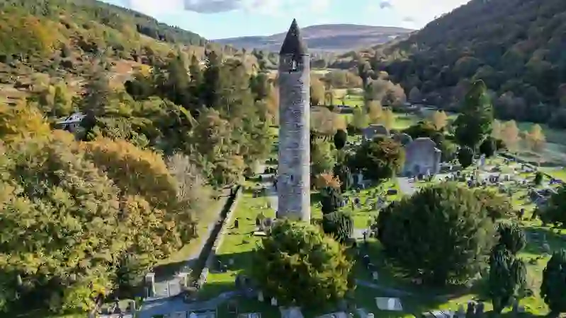 Glendalough round tower and cathedral ruins among autumn trees in Wicklow Mountains National Park.