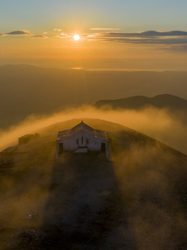 Puesta de sol sobre la cima del Croagh Patrick, con la capilla envuelta en niebla y luz dorada.