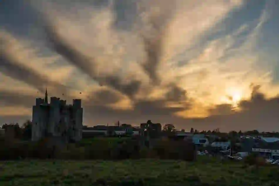 Trim Castle in County Meath rises above the surrounding town beneath a dramatic golden sunset and sweeping clouds.