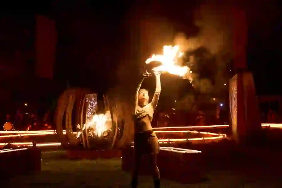 Performer raises flaming props during a night-time fire ceremony, surrounded by glowing installations at the Púca Festival.