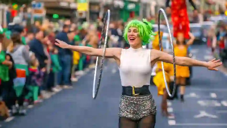 Drei Teilnehmer mit bunten Perücken und bemalten Gesichtern lächeln während einer St. Patrick's Day-Parade in Irland.