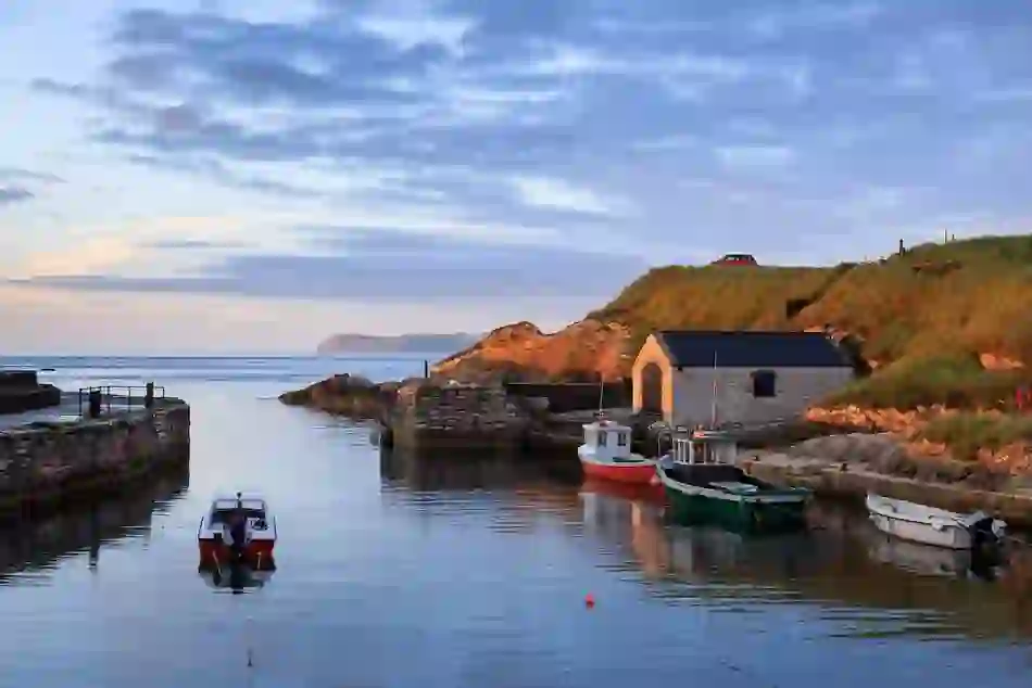 Small boats moored in Ballintoy Harbour, County Antrim, with a white boathouse and calm sea.