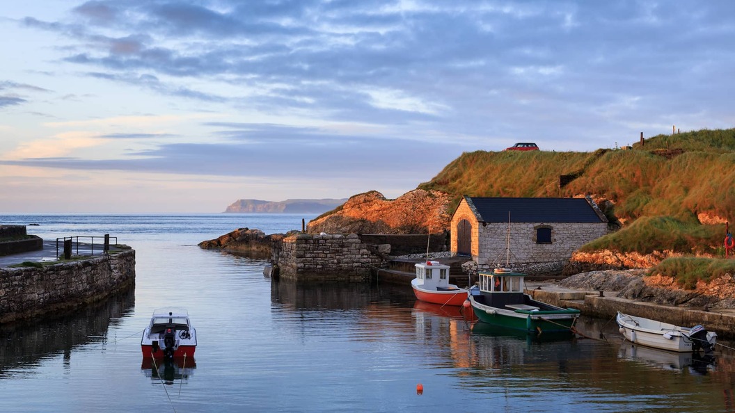 Small boats moored in Ballintoy Harbour, County Antrim, with a white boathouse and calm sea.