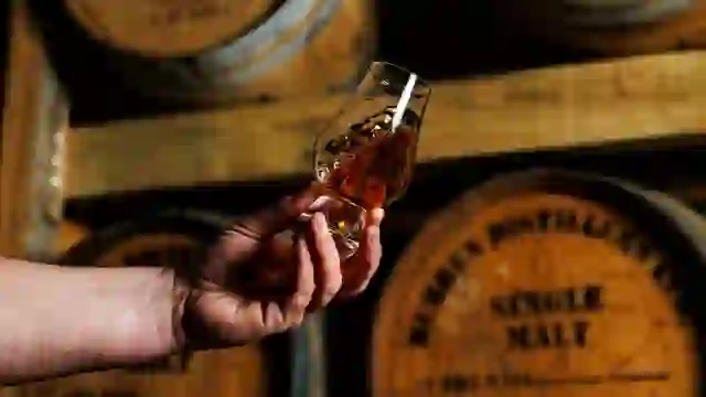 Hand holding a glass of Burren Distillers single malt whiskey in a barrel warehouse in County Clare.