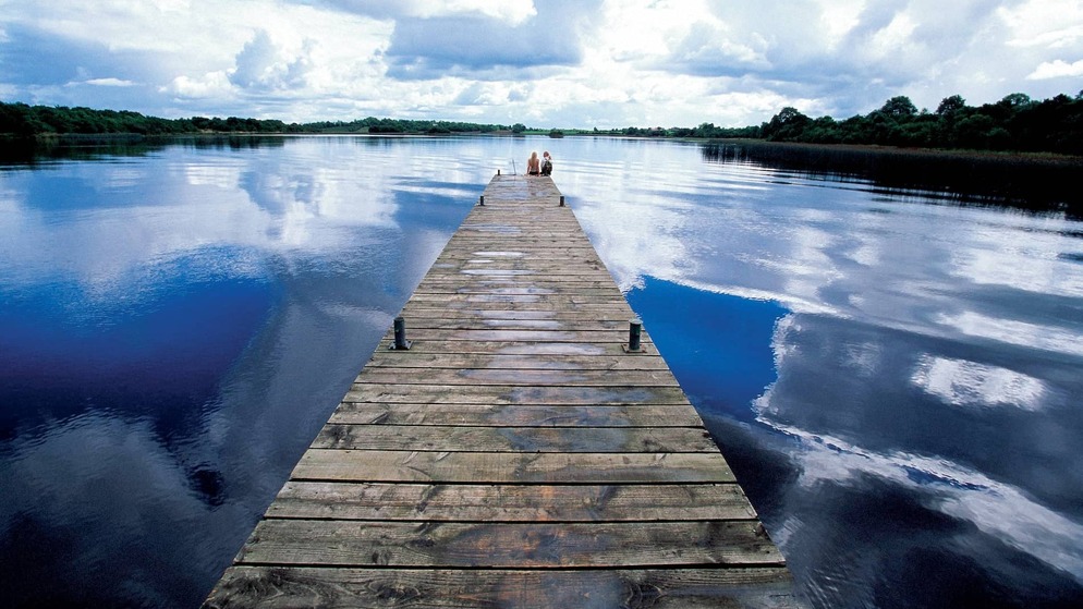 Wooden jetty stretching into the calm waters of Lough Erne in County Fermanagh beneath dramatic reflected skies.