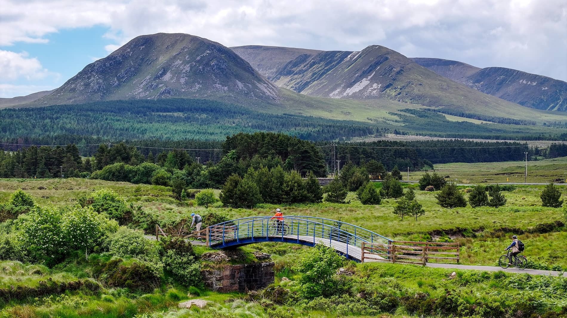 Cyclists cross a bridge on the Great Western Greenway with Croagh Patrick in County Mayo beyond.