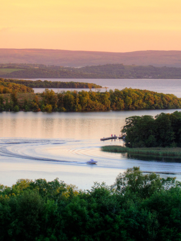 Motorboats create sweeping wakes across Lough Erne at sunset, surrounded by wooded islands in County Fermanagh.