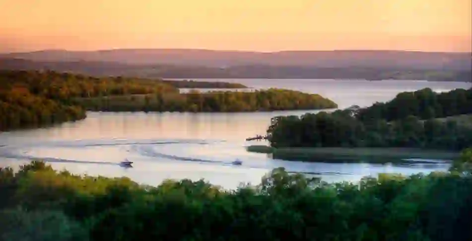 Motorboats create sweeping wakes across Lough Erne at sunset, surrounded by wooded islands in County Fermanagh.