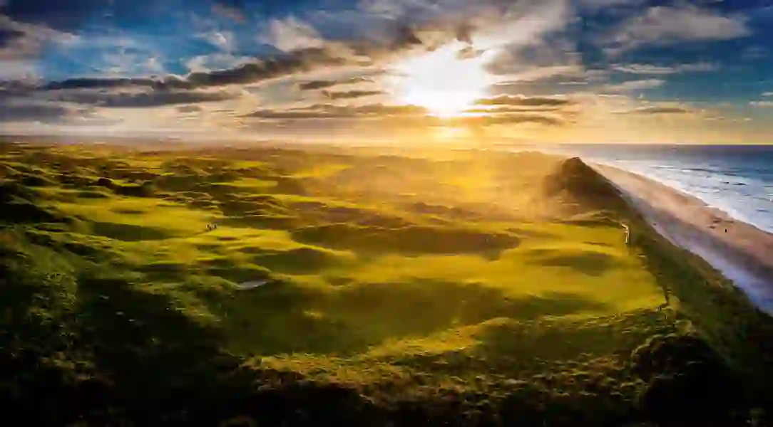 Golden sunlight casts long shadows across Royal Portrush Golf Course and the nearby beach on Antrim’s dramatic coastline.