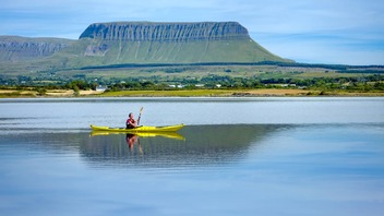 Person kayaking on calm water with Benbulben mountain in the background, County Sligo.