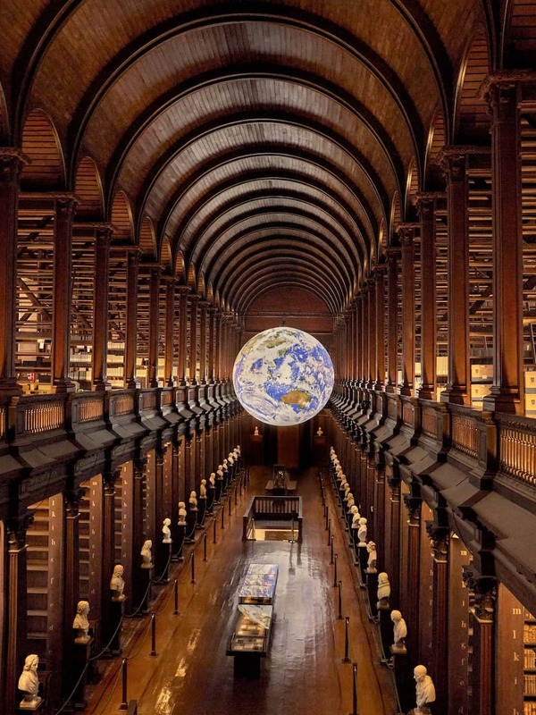 Grand vaulted Long Room at Trinity College Dublin with wooden arches, book-lined galleries, and a suspended illuminated globe.