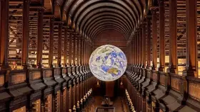Grand vaulted Long Room at Trinity College Dublin with wooden arches, book-lined galleries, and a suspended illuminated globe.