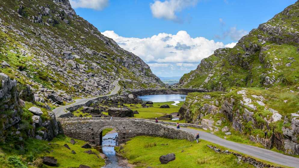 Eine kurvenreiche Straße und ein See führen durch das Gap of Dunloe in der Grafschaft Kerry, unter steilen, grünen Hängen.