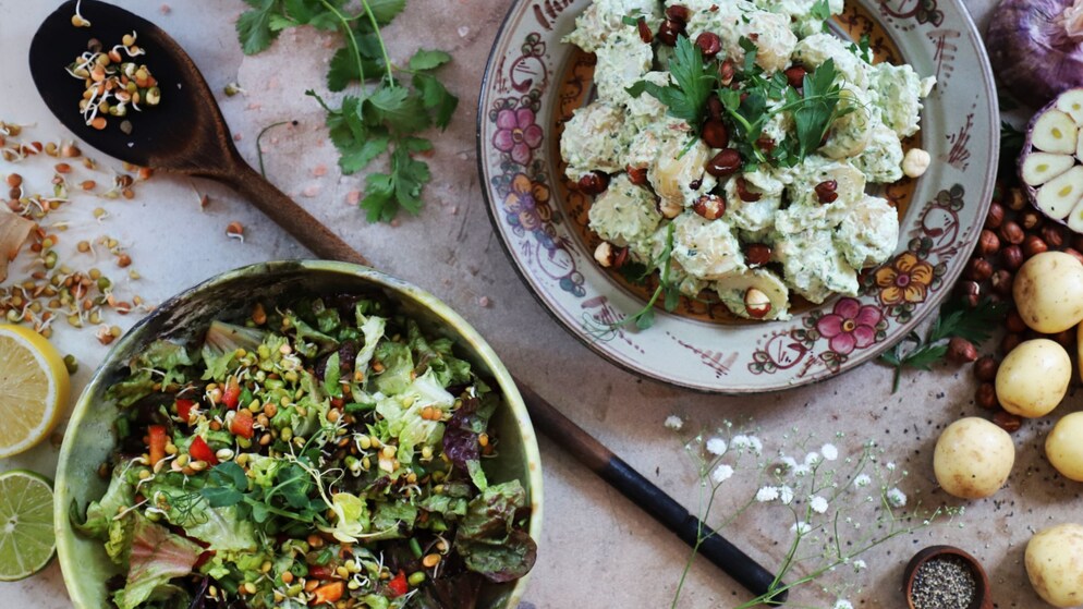Potato salad with hazelnuts and parsley on a floral plate, surrounded by fresh ingredients.