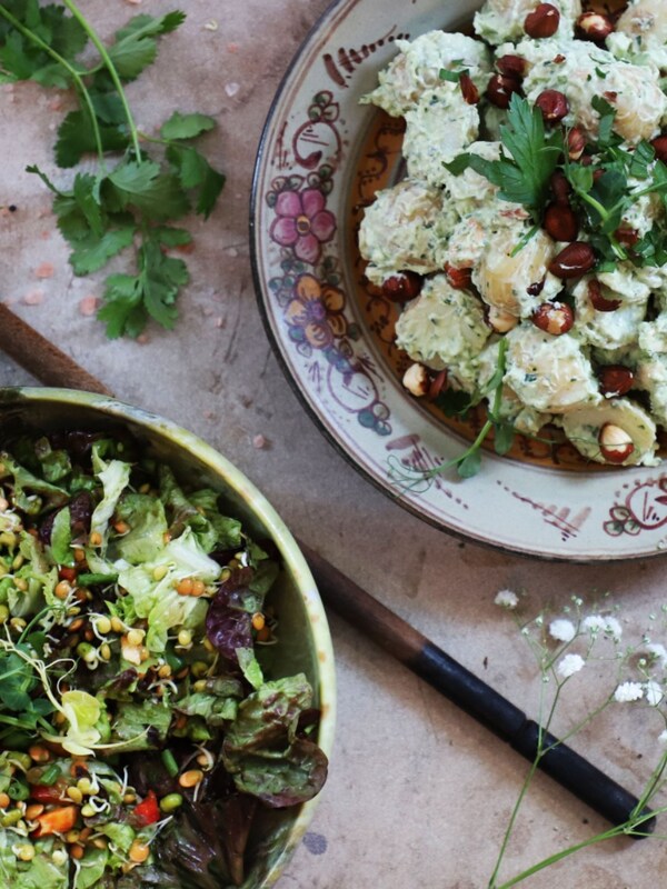 Aardappelsalade met hazelnoten en peterselie op een bord met bloemen, omringd door verse ingrediënten.