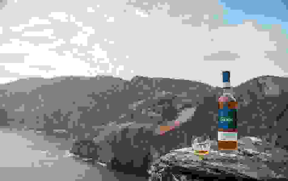 Bottle and glass of Silkie Irish whiskey at the Slieve League Cliffs in Donegal with ocean and mountains in the background.