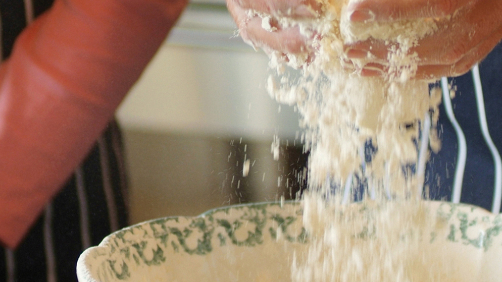 Eine Hand streut Mehl in eine Rührschüssel während des Knetens von traditionellem irischem Brot.