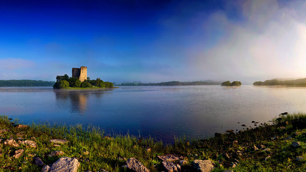 Sonnenaufgang über Lough Key, Grafschaft Roscommon, mit einer mittelalterlichen Burgruine auf einer kleinen Insel, umgeben von ruhigem Wasser.